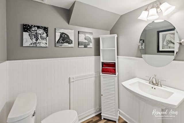 bathroom with a wainscoted wall, toilet, wood finished floors, and vaulted ceiling