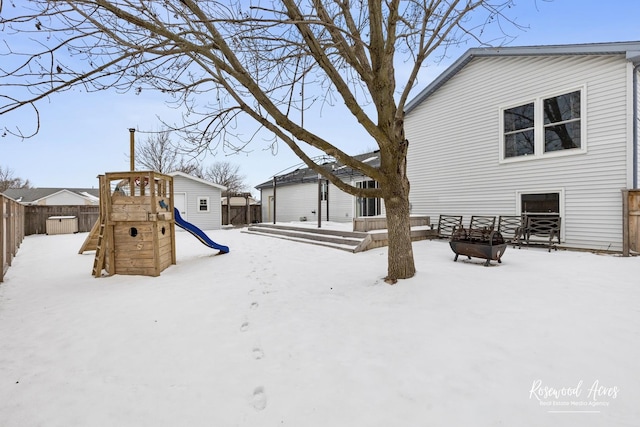 yard layered in snow with a playground and a fenced backyard