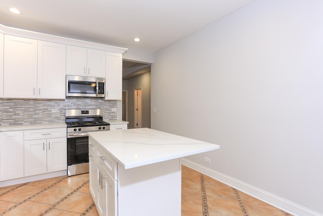 kitchen featuring light tile patterned floors, appliances with stainless steel finishes, white cabinetry, backsplash, and a kitchen island