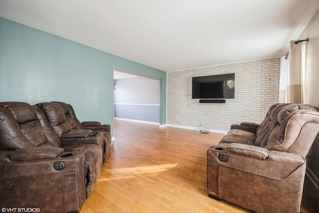 living area featuring brick wall, light wood-style flooring, and baseboards