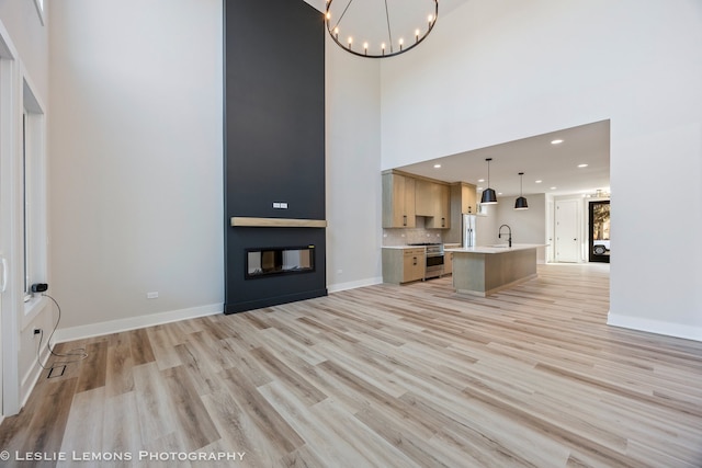 unfurnished living room featuring sink, an inviting chandelier, light wood-type flooring, a towering ceiling, and a fireplace