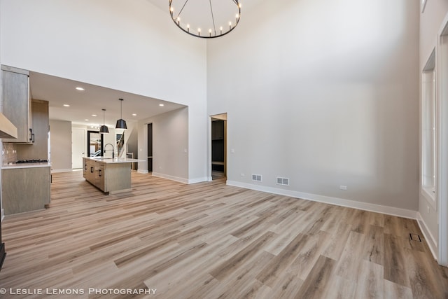 unfurnished living room with sink, light hardwood / wood-style floors, a high ceiling, and a notable chandelier