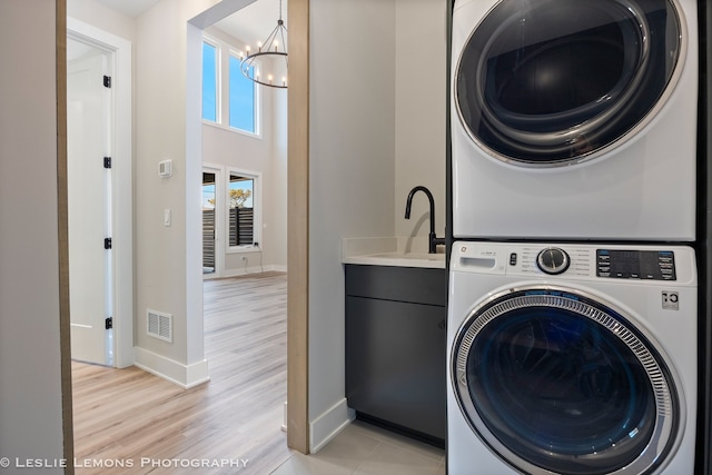 laundry room featuring a towering ceiling, stacked washer and dryer, cabinets, a notable chandelier, and light wood-type flooring