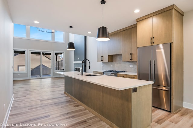 kitchen with stainless steel refrigerator, sink, backsplash, hanging light fixtures, and a center island with sink