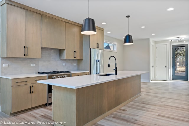 kitchen featuring light brown cabinetry, hanging light fixtures, a center island with sink, and appliances with stainless steel finishes