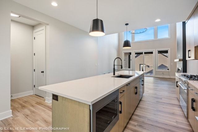 kitchen with sink, stainless steel stove, a kitchen island with sink, decorative light fixtures, and light wood-type flooring