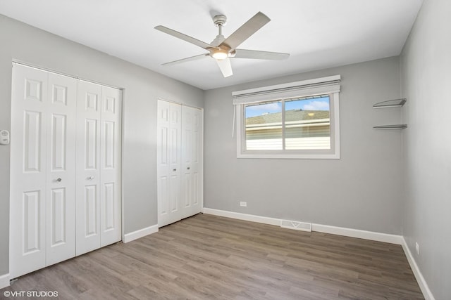 unfurnished bedroom featuring wood finished floors, two closets, visible vents, and baseboards