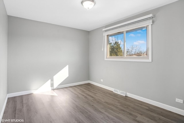 spare room with dark wood-type flooring, visible vents, and baseboards