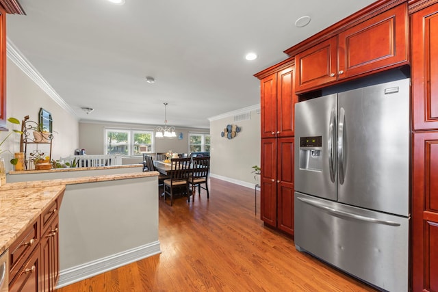 kitchen with light stone counters, light hardwood / wood-style flooring, ornamental molding, stainless steel fridge, and pendant lighting