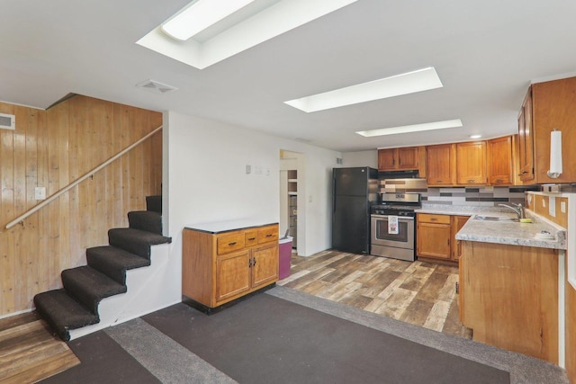 kitchen with dark wood-type flooring, stainless steel gas range, sink, black refrigerator, and wooden walls