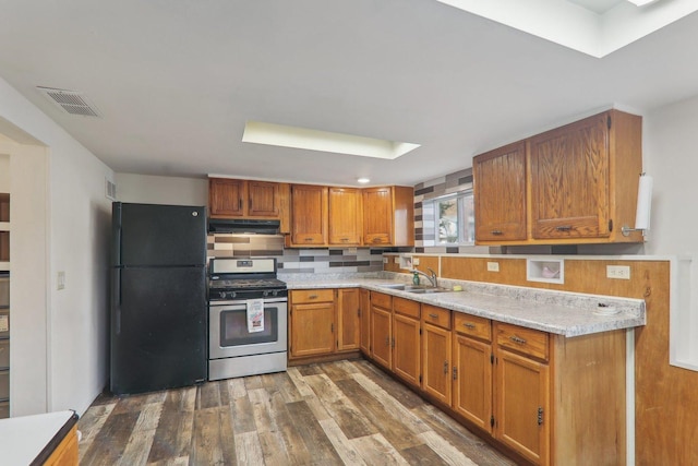 kitchen with sink, dark wood-type flooring, black refrigerator, stainless steel range with gas stovetop, and light stone countertops