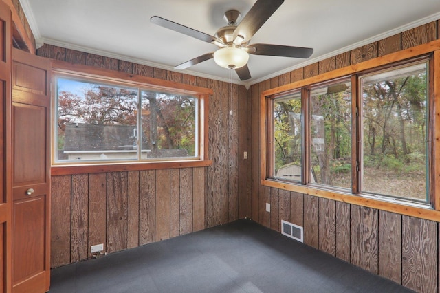 carpeted empty room with ceiling fan, ornamental molding, and wood walls