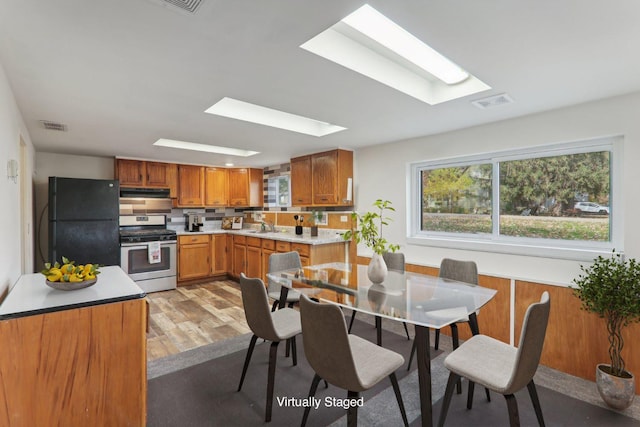 kitchen featuring sink, a skylight, stainless steel range with gas stovetop, black fridge, and light wood-type flooring