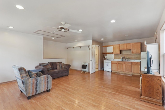 living room featuring ceiling fan, sink, heating unit, and light wood-type flooring