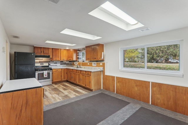 kitchen featuring backsplash, light hardwood / wood-style floors, black fridge, gas range, and kitchen peninsula