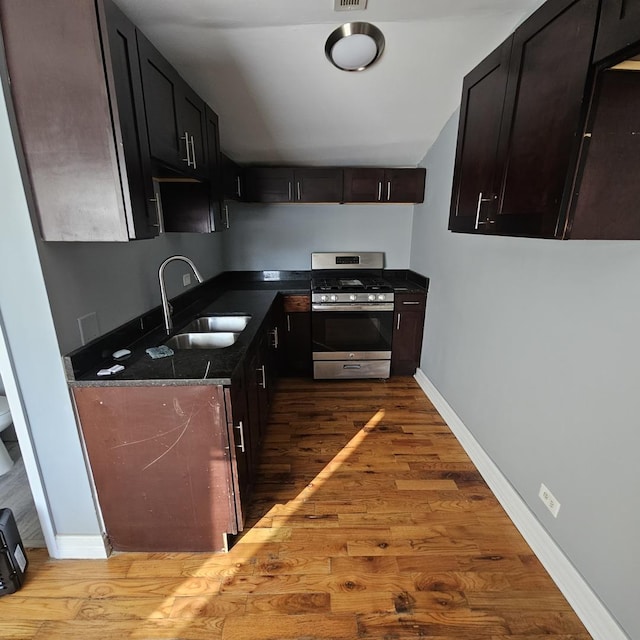 kitchen with sink, dark stone counters, stainless steel range with gas stovetop, and light hardwood / wood-style flooring