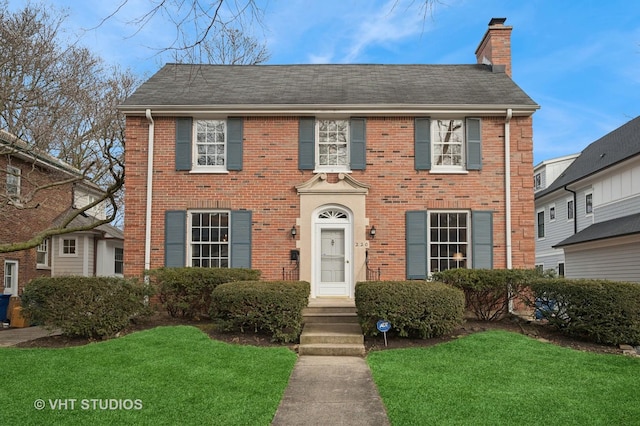 colonial home with a front yard, a chimney, and brick siding