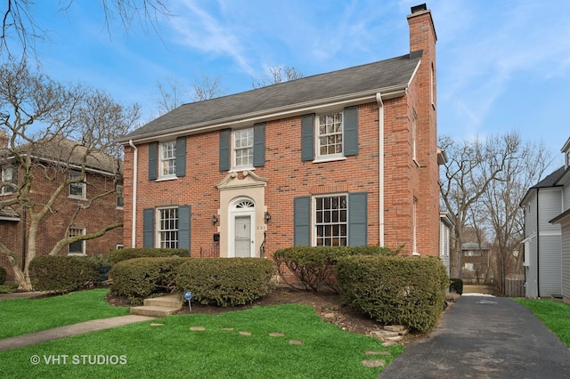 view of front of property with brick siding, a chimney, and a front lawn