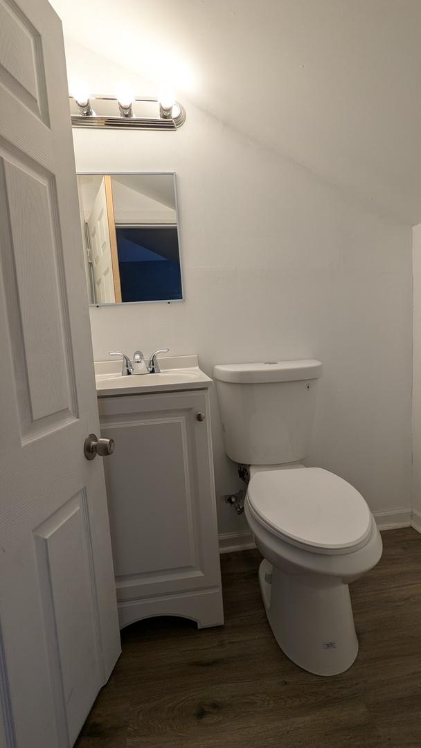 bathroom featuring hardwood / wood-style flooring, vaulted ceiling, vanity, and toilet