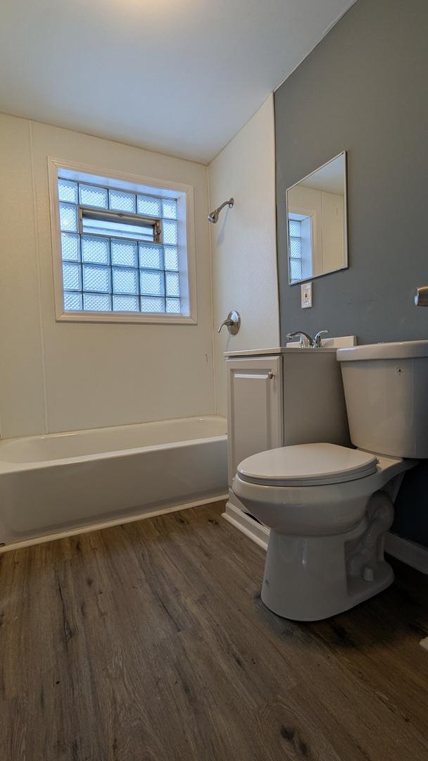 bathroom featuring hardwood / wood-style flooring, shower / bathtub combination, and toilet