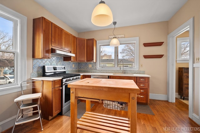 kitchen featuring tasteful backsplash, brown cabinetry, stainless steel range with gas stovetop, a sink, and under cabinet range hood