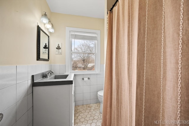 bathroom with tile patterned flooring, toilet, vanity, tile walls, and wainscoting