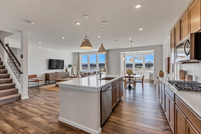 kitchen featuring appliances with stainless steel finishes, sink, dark hardwood / wood-style flooring, hanging light fixtures, and a kitchen island with sink