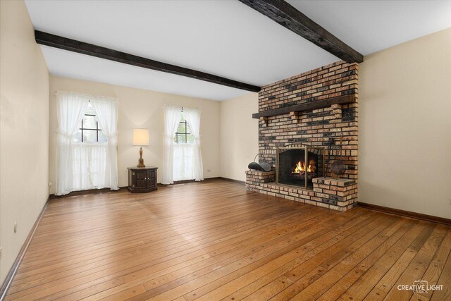 unfurnished living room with beam ceiling, hardwood / wood-style floors, a brick fireplace, and baseboards