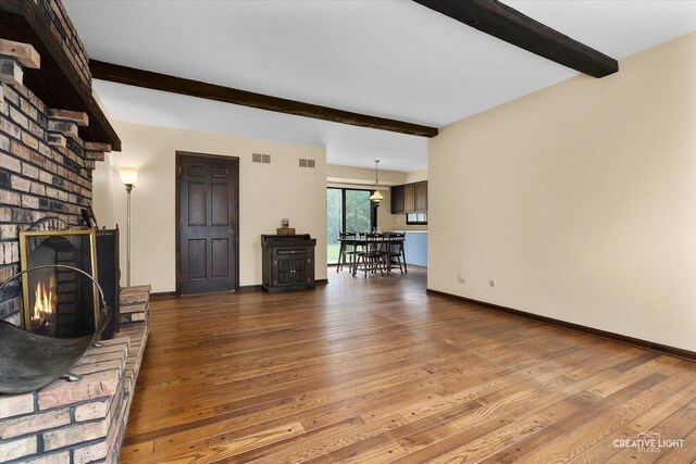 unfurnished living room with beamed ceiling, hardwood / wood-style flooring, a fireplace, and baseboards