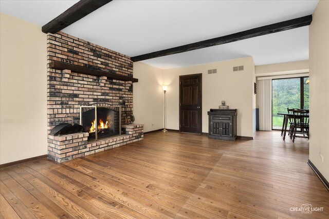unfurnished living room featuring beamed ceiling, hardwood / wood-style flooring, a brick fireplace, and baseboards