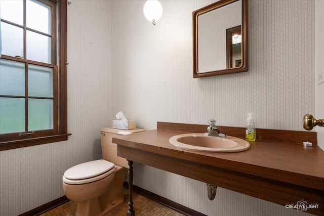 half bath featuring a sink, plenty of natural light, wallpapered walls, toilet, and baseboards