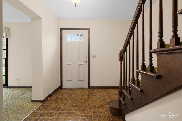 carpeted foyer featuring stairs and baseboards