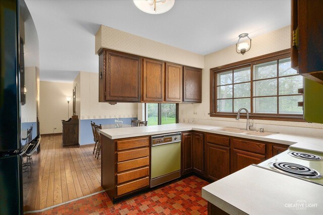 kitchen with freestanding refrigerator, dishwashing machine, a sink, light countertops, and a peninsula