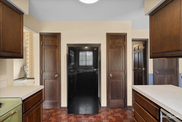 kitchen with freestanding refrigerator, light countertops, wallpapered walls, brick patterned floors, and dark brown cabinets
