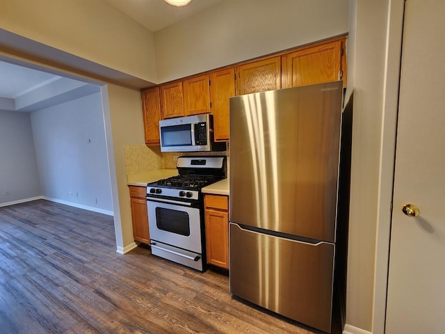 kitchen with stainless steel appliances, light countertops, backsplash, dark wood-style floors, and brown cabinetry