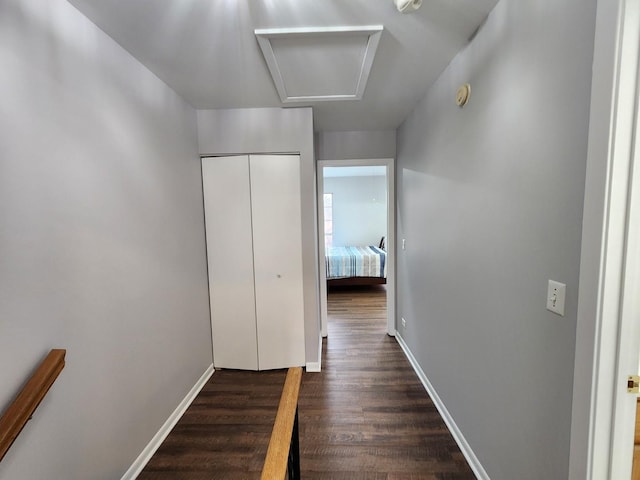 corridor featuring attic access, baseboards, and dark wood-style flooring