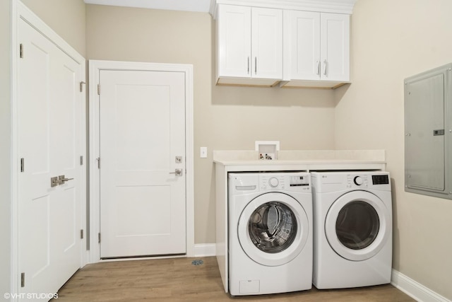 clothes washing area featuring cabinets, washing machine and clothes dryer, electric panel, and light hardwood / wood-style flooring