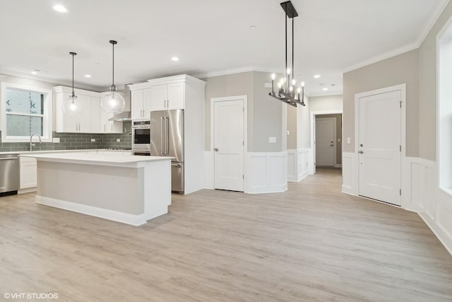 kitchen with appliances with stainless steel finishes, a kitchen island, decorative light fixtures, white cabinets, and crown molding