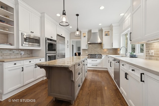 kitchen featuring white cabinets, built in appliances, a kitchen island, and wall chimney range hood