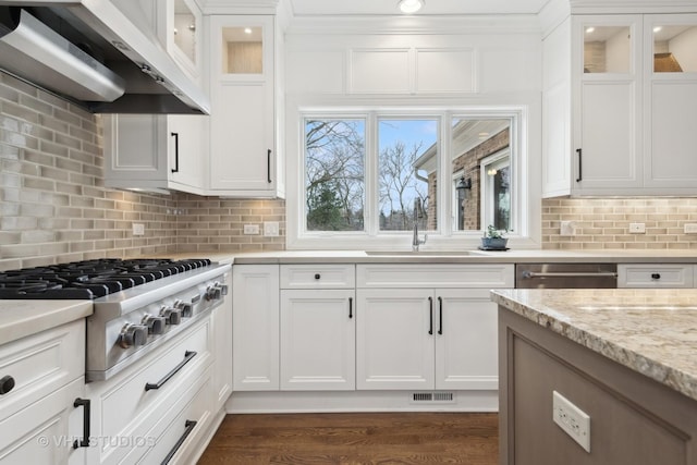 kitchen with wall chimney exhaust hood, sink, white cabinetry, appliances with stainless steel finishes, and light stone countertops