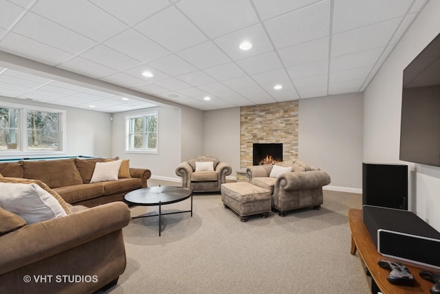 living room with a stone fireplace, carpet floors, and a drop ceiling