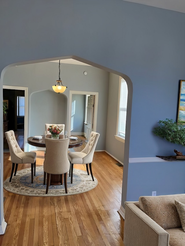 dining room with baseboards, arched walkways, and light wood-style floors