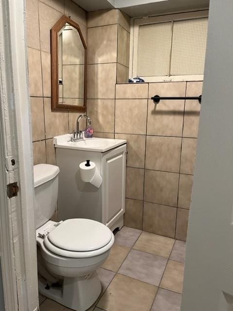 half bathroom with tile patterned flooring, toilet, tile walls, and vanity