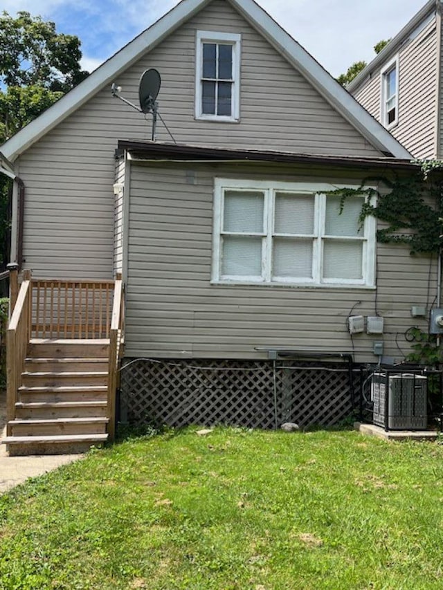 rear view of house with central AC unit and a lawn