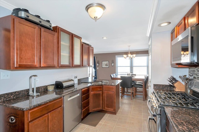 kitchen with dark stone counters, glass insert cabinets, decorative light fixtures, a peninsula, and stainless steel appliances