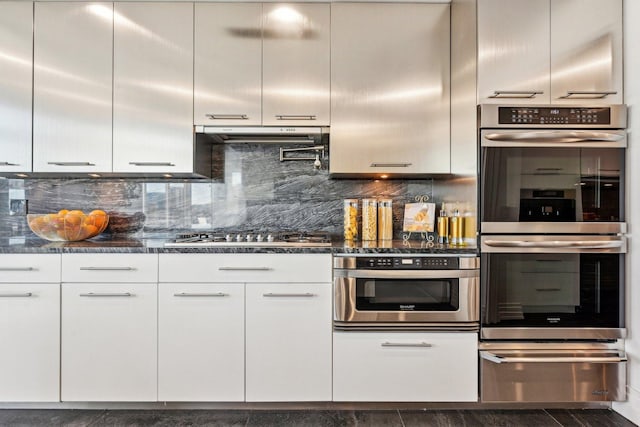 kitchen featuring a warming drawer, under cabinet range hood, tasteful backsplash, white cabinetry, and appliances with stainless steel finishes