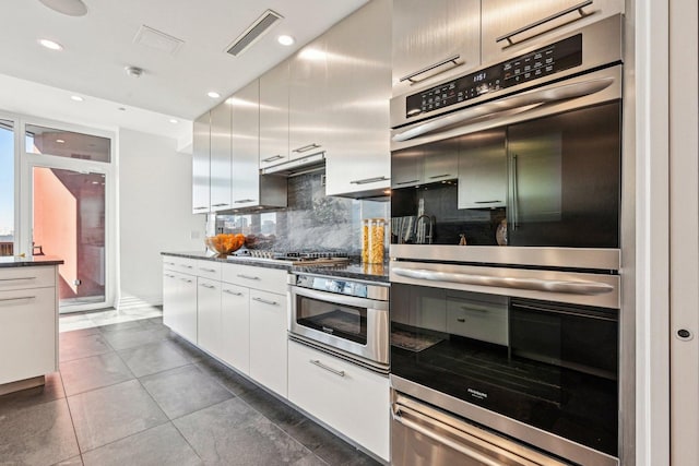 kitchen featuring visible vents, backsplash, dark countertops, refrigerator, and white cabinetry