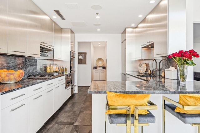 kitchen with visible vents, a peninsula, a sink, appliances with stainless steel finishes, and a kitchen breakfast bar