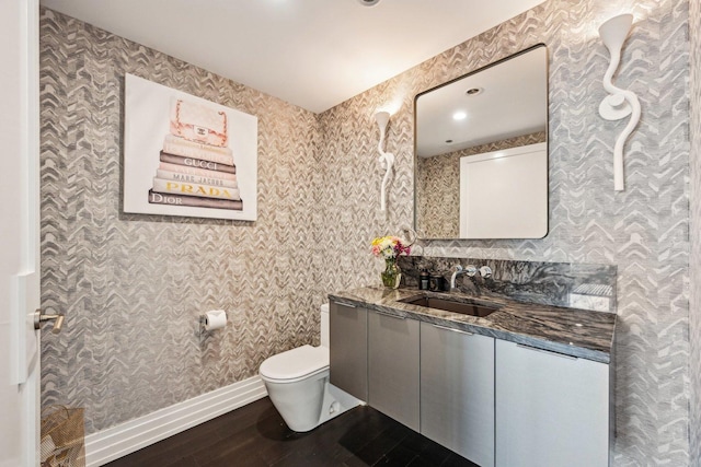 bathroom with vanity, wood finished floors, baseboards, wallpapered walls, and toilet