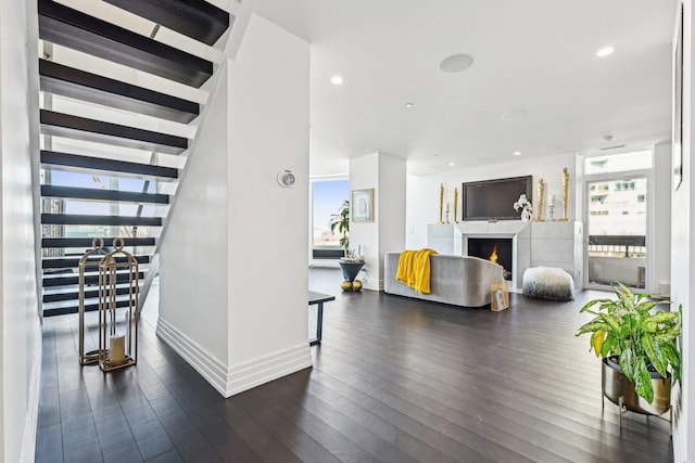 living area with dark wood-style floors, baseboards, recessed lighting, a warm lit fireplace, and stairs